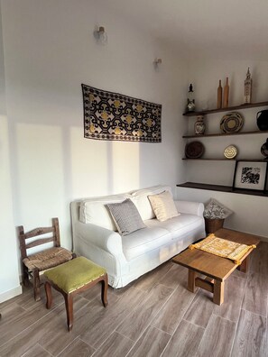 Ein Wohnzimmer mit einem weißen Sofa, einem Holzstuhl, einem kleinen Tisch und einem Regal mit Dekoration.