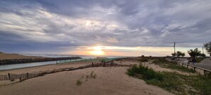 Ein Strand mit einer Holzbrüstung, einem Felsstollen und einem Sonnenuntergang.