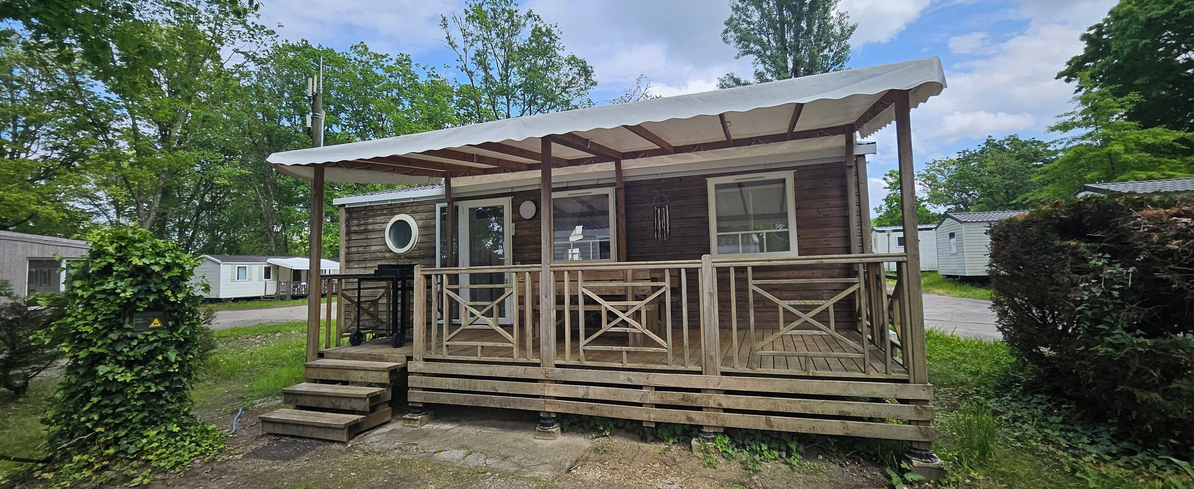 Een houten blokhut met een veranda, een rond raam en een deur.
