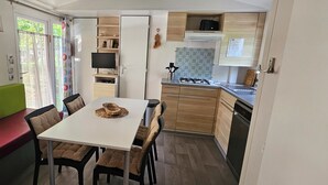 Une cuisine de taille réduite comprenant un coin repas, un téléviseur et une fenêtre avec des rideaux.