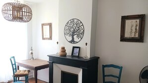 Ein Zimmer mit Kamin, Esstisch, Stühlen, einer Pendelleuchte und Wandbildern.