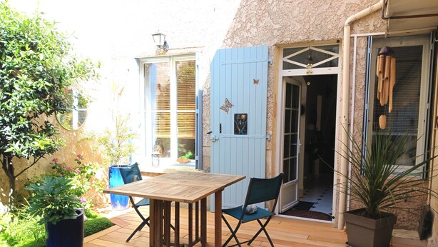 Eine Terrasse im Freien mit einem Holztisch und -stühlen, einem Blumentopf und einer blauen Tür, die zu einem Raum führt.
