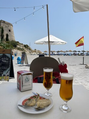 Une table avec un repas, deux verres de bière et un panneau affichant le menu dans un restaurant situé en bord de plage.