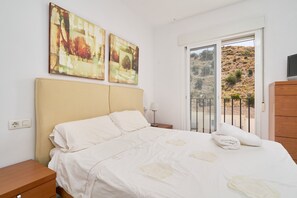 A bedroom with a bed, a nightstand, a lamp, and a view of a hillside through a sliding door. - Casa Mamá: Sea Views, Private Pool & Wi-Fi on the Costa Tropical (Almuñécar)