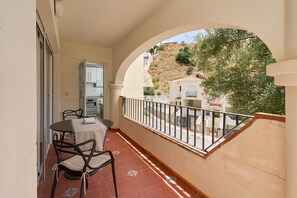 A balcony with a table and chairs, a view of a hillside, and a building with a tiled roof. - Casa Mamá: Sea Views, Private Pool & Wi-Fi on the Costa Tropical (Almuñécar)