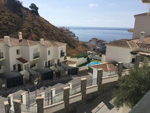 A coastal residential area with buildings featuring tiled roofs and balconies, a swimming pool, and a view of the sea. - Casa Mamá: Sea Views, Private Pool & Wi-Fi on the Costa Tropical (Almuñécar)