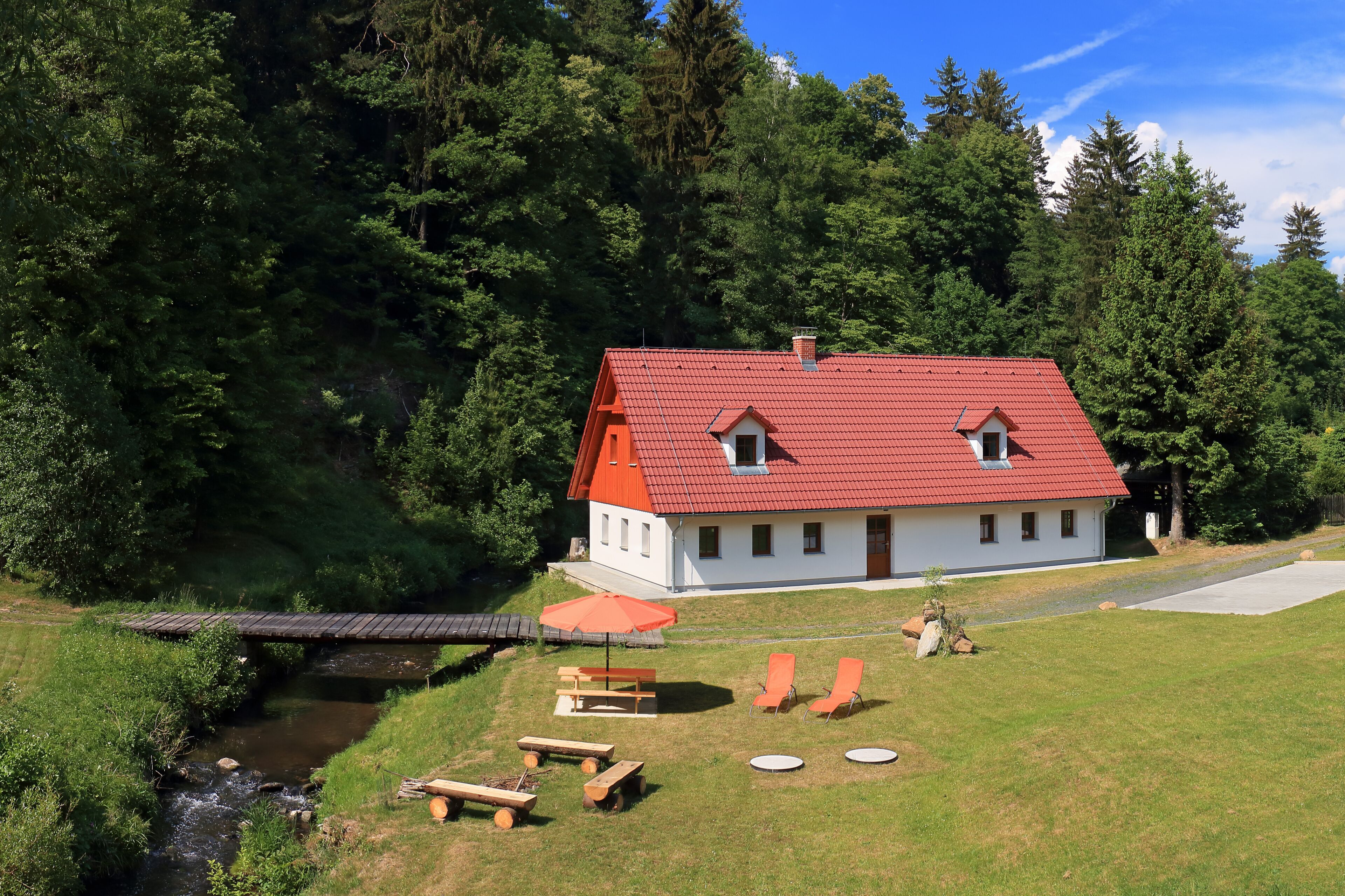 Ein Haus mit rotem Dach, einer kleinen Brücke und Sitzgelegenheiten im Freien.