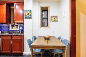 A kitchen with wooden cabinets and a blue tiled backsplash, a dining table with chairs, and a window with a view. - Enjoy Easy Access to the West side Manhattan (New York)
