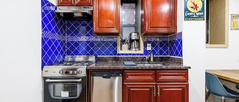 A kitchen with wooden cabinets, a stove, a dishwasher, and blue-tiled backsplash.