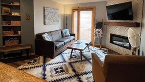 Una sala de estar con sofá, mesa de centro, televisor, chimenea y un tapete estampado.