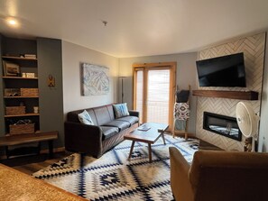A living room with a sofa, coffee table, TV, fireplace, and a patterned rug. - Convenience and Amenities in the Resort Base (Taos Ski Valley)