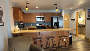 Una cocina moderna con armarios de madera, un refrigerador de acero inoxidable, una estufa a gas y una barra con taburetes.
