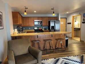 A modern kitchen with wooden cabinets, a stainless steel refrigerator, a gas stove, and a bar area with stools. - Convenience and Amenities in the Resort Base (Taos Ski Valley)