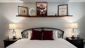 Habitación de hotel con una cama grande, dos lámparas de noche, una mesita de noche con un pañuelero y tres cuadros en la pared.