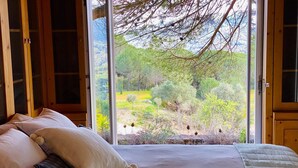 A bedroom with a large window, a bed with pillows, and a view of a garden. - Quinta da Rampa - Arrábida (Azeitão)
