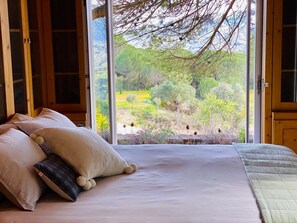 A bedroom with a large window, a bed with pillows, and a view of a garden. - Quinta da Rampa - Arrábida (Azeitão)