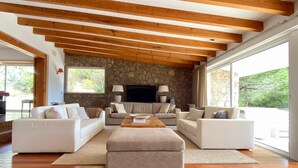 A spacious living room with a stone wall, wooden beams, and large windows. - Quinta da Rampa - Arrábida (Azeitão)