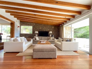 A spacious living room with a stone wall, wooden beams, and large windows. - Quinta da Rampa - Arrábida (Azeitão)