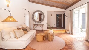 Uma sala de estar com um sofá branco, tabourets de madeira redondos, um espelho e um abajur.