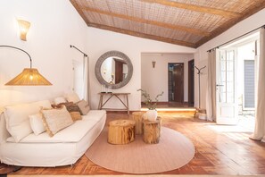 Een woonkamer met een witte bank, ronde houten krukken, een spiegel en een lamp.