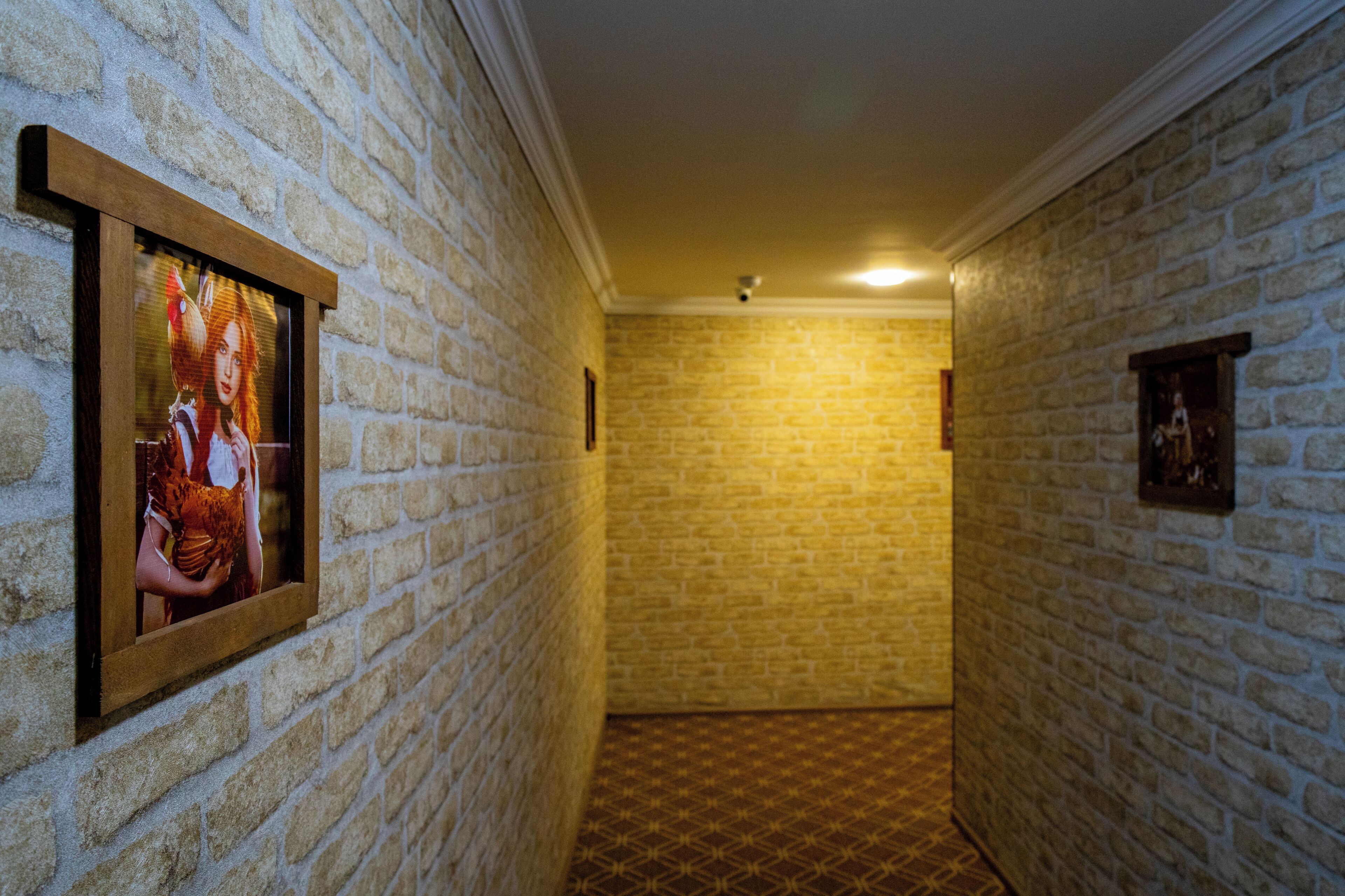 A hallway with brick walls and a patterned floor, leading to a room with a framed picture on the wall.