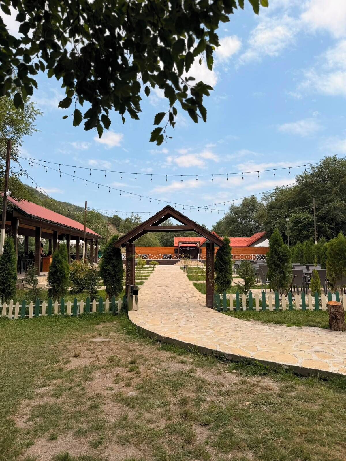 Un chemin menant à un bâtiment doté d’un toit rouge, entouré de verdure et d’une clôture blanche en bois.