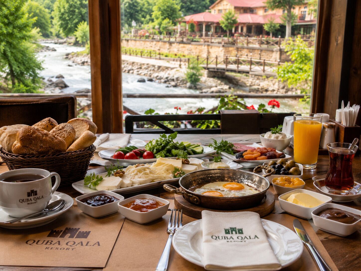 Una mesa de desayuno con diversos alimentos, una taza de café y vistas a un río y edificios.