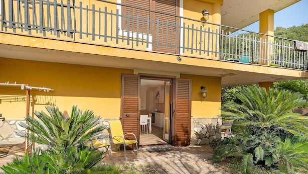 Un edificio giallo con un balcone, una porta e un piccolo giardino con palme.