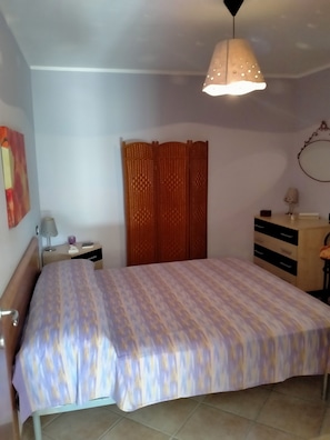 A bedroom with a bed, a nightstand, a lamp, a dresser, and a curtain. - La Grande Quercia, relaxation in the heart of Cilento (Perdifumo)