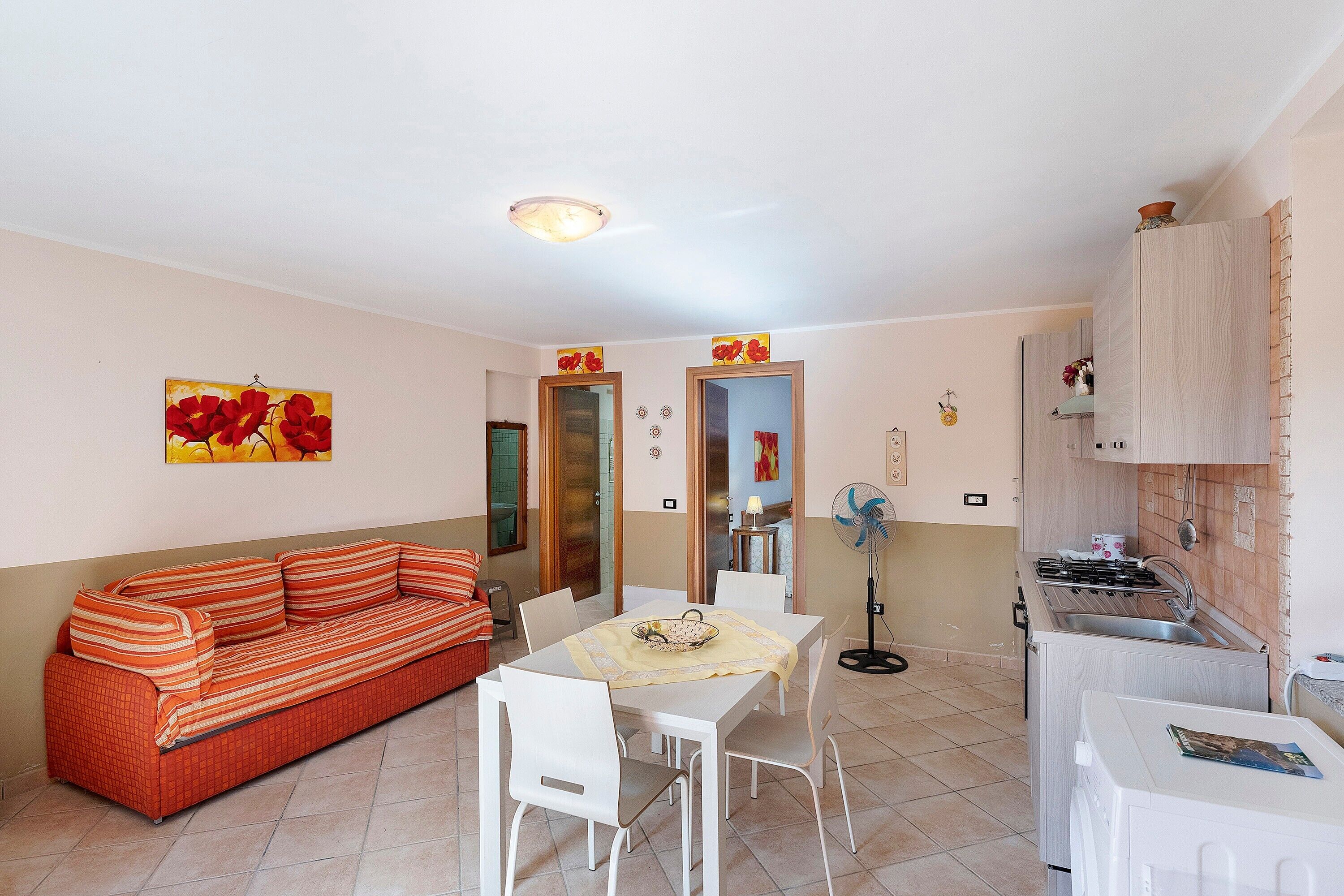 Un espace de vie compact comprenant un canapé, une table à manger, des chaises, un coin cuisine avec une cuisinière et un petit ventilateur.