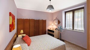 Una camera da letto con un letto, comodino, lampada, cassettiera, specchio e finestra.