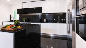 Una cocina moderna con encimeras negras, electrodomésticos de acero inoxidable y una isla central con frutas y verduras frescas.