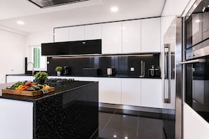 A modern kitchen with black countertops, stainless steel appliances, and a central island with fresh produce. - Villa Magali – Swimming pool, golf and beach (Charneca de Caparica)