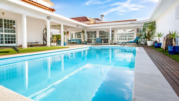 Una piscina con sillas de descanso, un porche cubierto y vistas a un edificio con grandes ventanales.