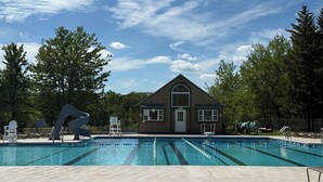 A swimming pool with clear lanes, a building with a gabled roof, and trees in the background. - Perfect Pocono Retreat / Golf / FirePit /Swimming Pool/BBQ near Waterparks (Tobyhanna)