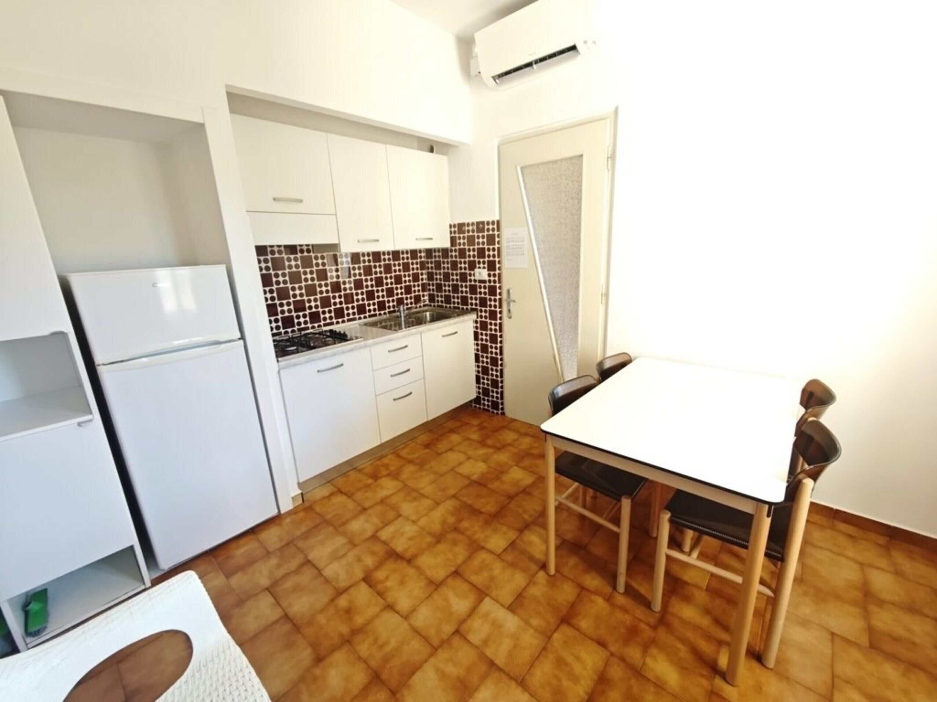 A compact kitchen with white cabinets, a tiled backsplash, a dining table with chairs, and a built-in stove.