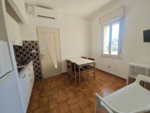 Eine kompakte Küche mit Esstisch und Stühlen, einem Fenster mit Jalousien und einer kleinen, weißen Ablagefläche.