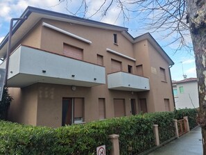 A two-story residential building with balconies, a gated entrance, and a hedge in front. - Apartment Close to sea and Centre (Lignano Sabbiadoro)