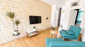Ein modernes Wohnzimmer mit einer Steinwand, einem Flachbildfernseher, zwei Zimmerpflanzen, einem türkisfarbenen Sofa und einem Couchtisch.