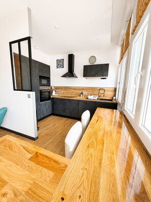 Une cuisine moderne avec une table à manger en bois, un four encastré et une hotte noire.