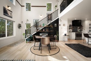 Eine moderne Küche mit schwarzem Fischgräten-Kochfeld, ein Essbereich mit rundem Tisch und Stühlen sowie eine Treppe, die in ein Obergeschoss führt.