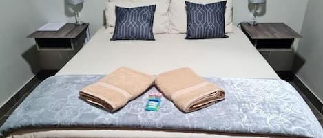 A hotel room with a bed, two bedside tables, two lamps, and towels on the bed.
