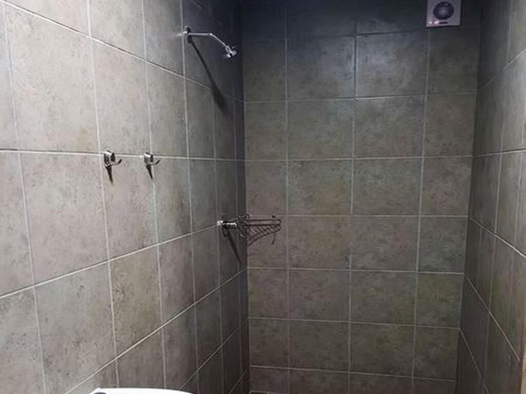 Une cabine de douche carrelée, dotée d’un pommeau de douche à main et d’un robinet fixé au mur.