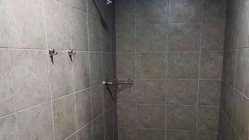 Une cabine de douche carrelée, dotée d’un pommeau de douche à main et d’un robinet fixé au mur.