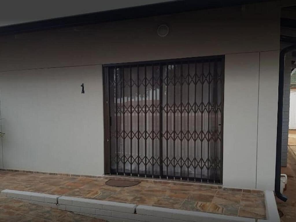 Una entrada con portón cerrado, el número '1' en la pared, adoquinado y reja metálica.