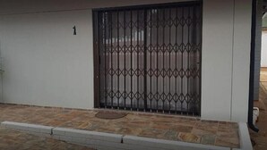 Una entrada con portón cerrado, el número '1' en la pared, adoquinado y reja metálica.