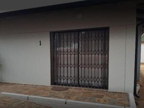 Una entrada con portón cerrado, el número '1' en la pared, adoquinado y reja metálica.