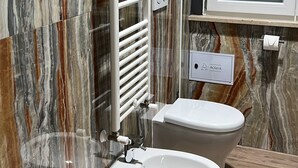 Un bagno con due servizi igienici, un lavandino bianco, un porta asciugamani e un porta carta igienica.