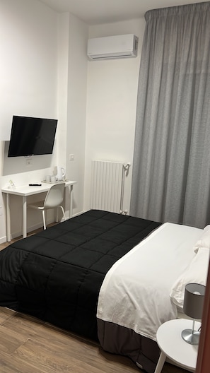 Ein Hotelzimmer mit Bett, Schreibtisch mit Stuhl, Fernseher, Heizkörper und einem Fenster mit Vorhängen.