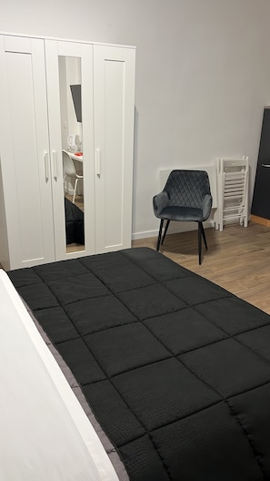 Una habitació amb llit, cadira, armari i escriptori.